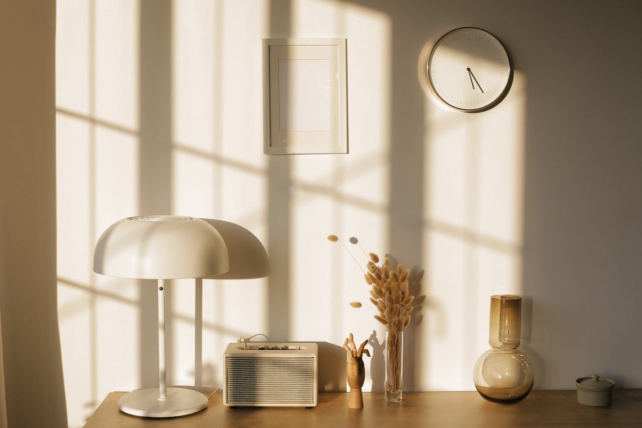 Light room with retro radio and decorative vases with dry plants on desk near wall with clock and window shadow in sunlight